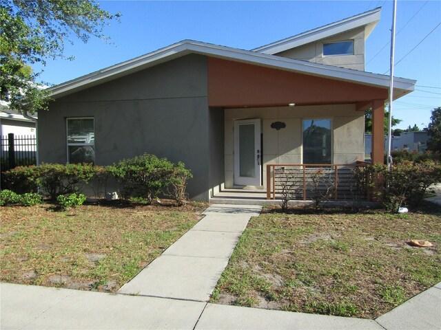 view of front facade with a porch, a front lawn, fence, and stucco siding