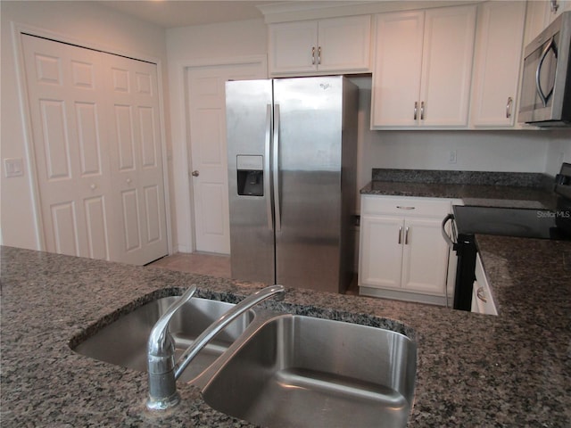 kitchen featuring white cabinets, appliances with stainless steel finishes, dark stone counters, and a sink