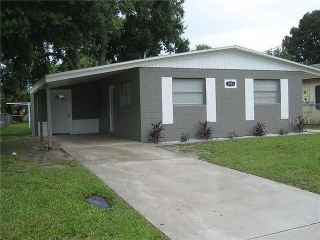 view of front of home with concrete driveway, concrete block siding, an attached carport, and a front lawn
