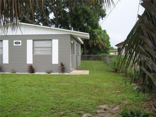 view of property exterior with a yard, concrete block siding, and fence