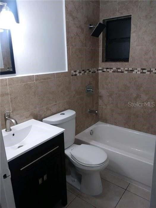 full bathroom with vanity, toilet, shower / bath combination, tile walls, and tile patterned floors