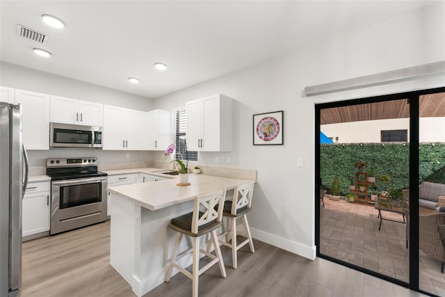 549 NE 206th Ln, Miami, FL 33179 - kitchen featuring stainless steel appliances, visible vents, a peninsula, a kitchen bar, and white cabinetry