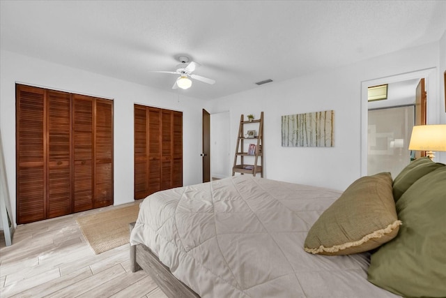 bedroom with two closets, a ceiling fan, visible vents, and light wood-style floors