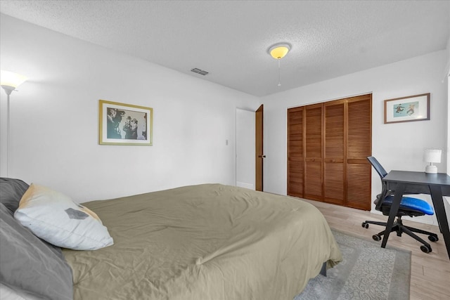 bedroom with visible vents, a closet, wood finished floors, and a textured ceiling