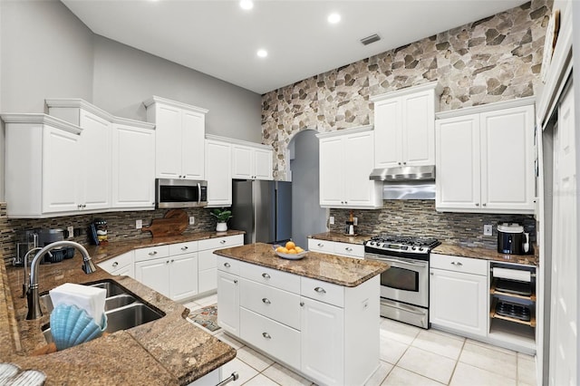 kitchen with stainless steel appliances, light tile patterned floors, decorative backsplash, a kitchen island, and arched walkways