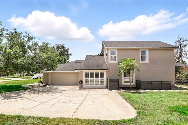 rear view of property featuring stucco siding, a garage, a lawn, driveway, and a patio area