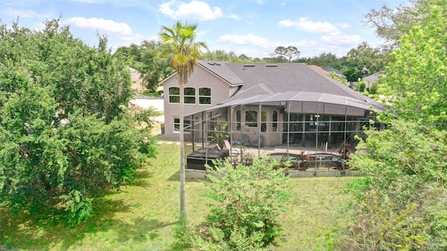 rear view of property with a yard, glass enclosure, stucco siding, and a patio area