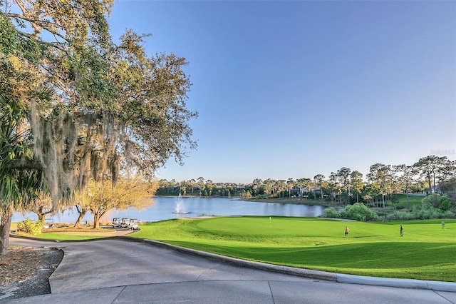 view of community featuring a water view, view of golf course, a lawn, and an area to practice putting