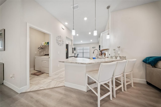 8137 Merano Ave, Fort Pierce, FL 34951 - kitchen featuring visible vents, a breakfast bar, a peninsula, white cabinetry, and washer / dryer