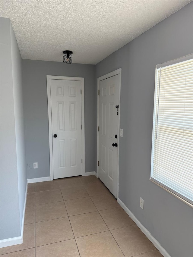 entryway featuring light tile patterned floors, a textured ceiling, and baseboards