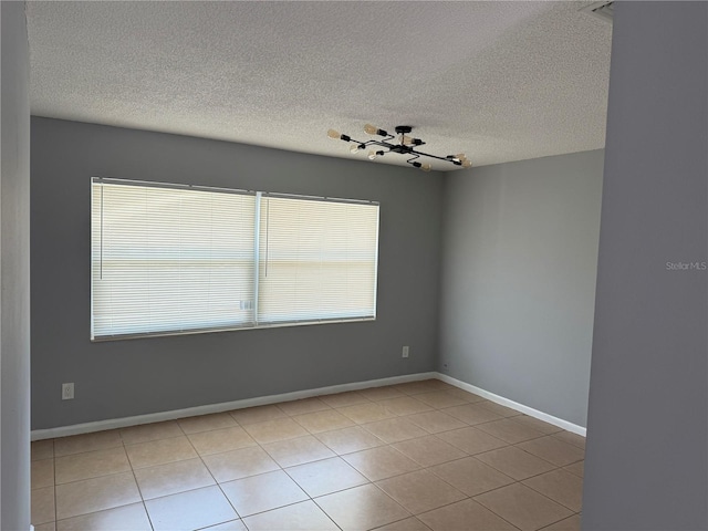 empty room with a textured ceiling, baseboards, and tile patterned flooring