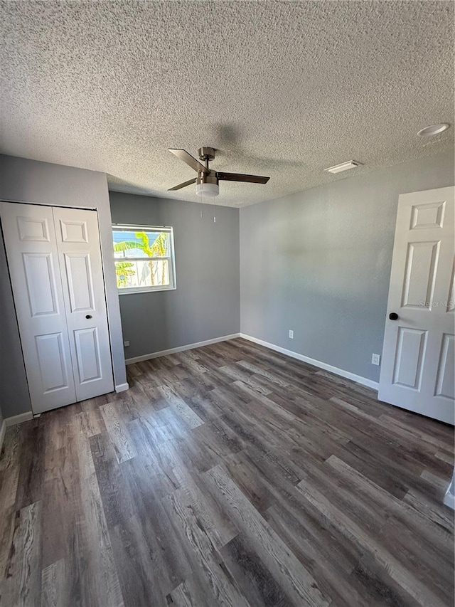 unfurnished bedroom with a closet, baseboards, dark wood-style floors, a textured ceiling, and a ceiling fan