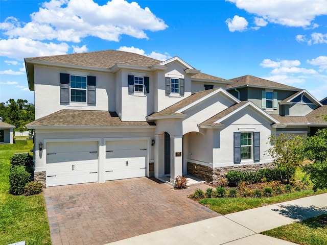 view of front of house with a shingled roof, an attached garage, stone siding, stucco siding, and decorative driveway