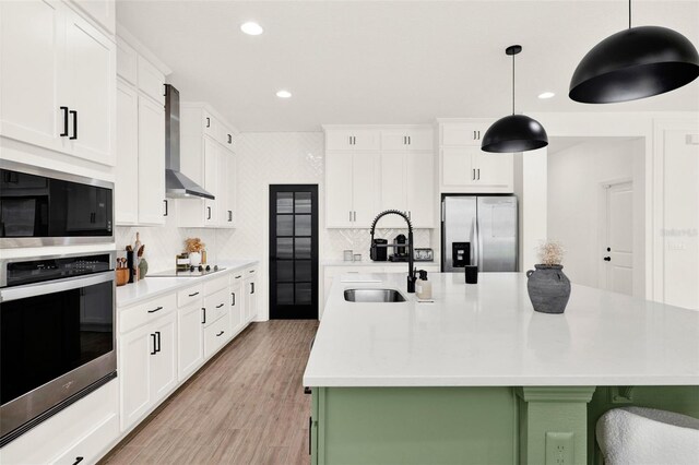 kitchen featuring wall chimney exhaust hood, recessed lighting, light countertops, a sink, and stainless steel appliances