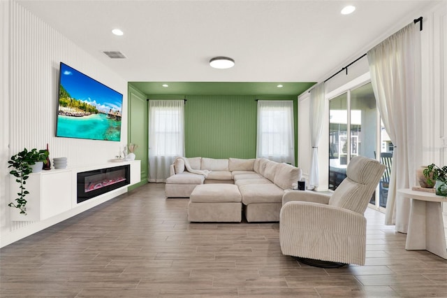 living area with a glass covered fireplace, visible vents, an accent wall, and wood finished floors