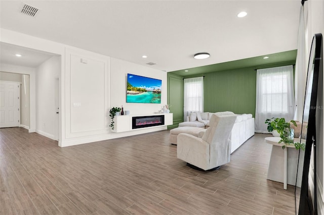 living area featuring a glass covered fireplace, visible vents, recessed lighting, wood finished floors, and baseboards
