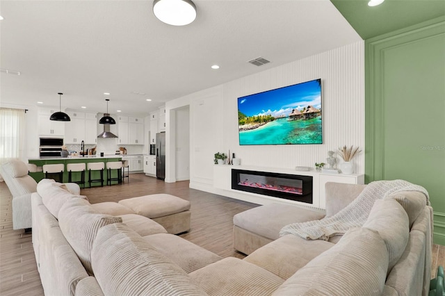 living room with light wood-style flooring, a glass covered fireplace, visible vents, and recessed lighting