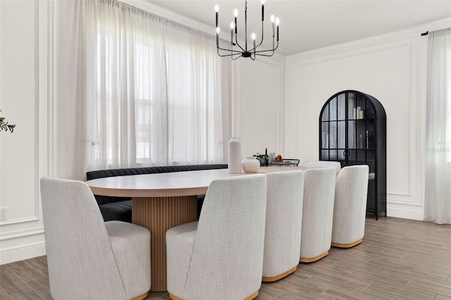 dining area featuring a decorative wall, light wood-type flooring, arched walkways, and a notable chandelier