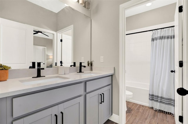 full bath featuring toilet, wood finished floors, double vanity, and a sink