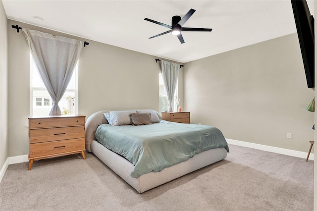 bedroom featuring light carpet, ceiling fan, baseboards, and multiple windows
