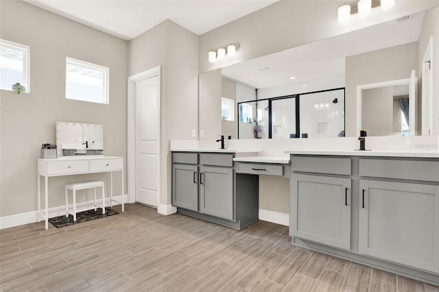 bathroom featuring baseboards, a sink, a shower stall, wood finished floors, and two vanities