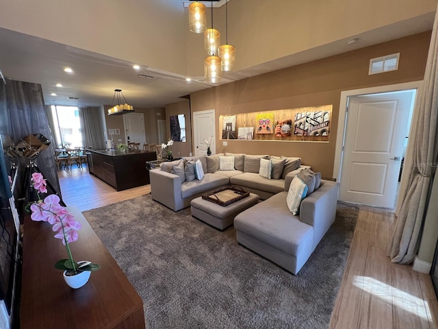 living area featuring visible vents, recessed lighting, a towering ceiling, and wood finished floors