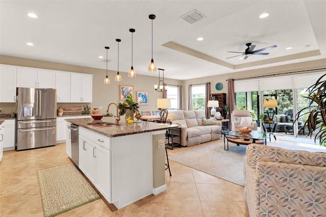 kitchen with dark stone countertops, a sink, open floor plan, appliances with stainless steel finishes, and a ceiling fan