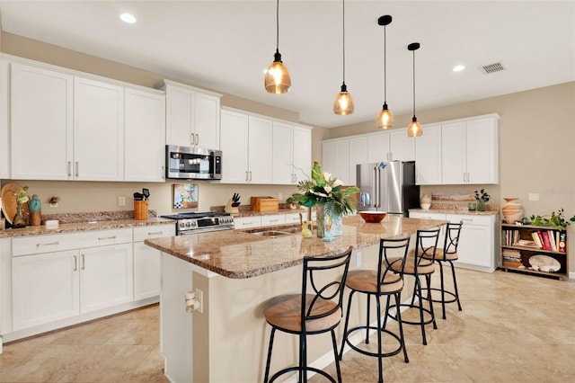 kitchen with a kitchen bar, white cabinetry, visible vents, a kitchen island with sink, and stainless steel appliances