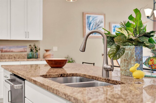 kitchen featuring light stone counters, a sink, and white cabinetry