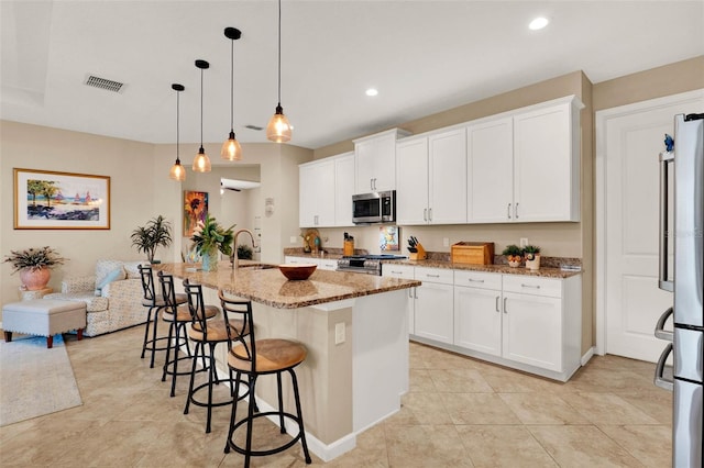kitchen with a breakfast bar, light stone countertops, visible vents, stainless steel appliances, and a sink
