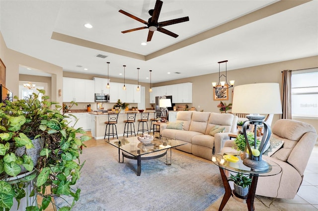 living room with recessed lighting, light tile patterned floors, visible vents, a raised ceiling, and ceiling fan with notable chandelier