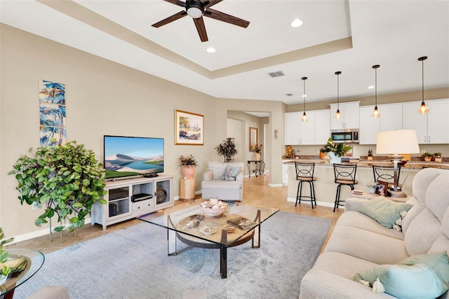 living area with a ceiling fan, visible vents, recessed lighting, a raised ceiling, and baseboards