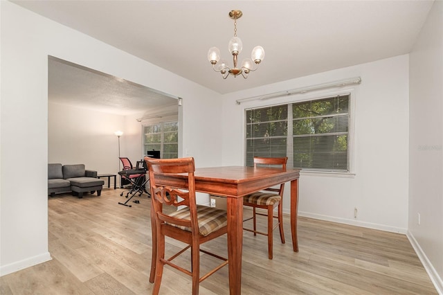 dining area with light wood-type flooring, baseboards, and an inviting chandelier
