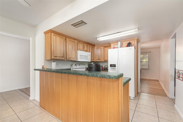 kitchen with dark countertops, visible vents, light tile patterned floors, white appliances, and a peninsula