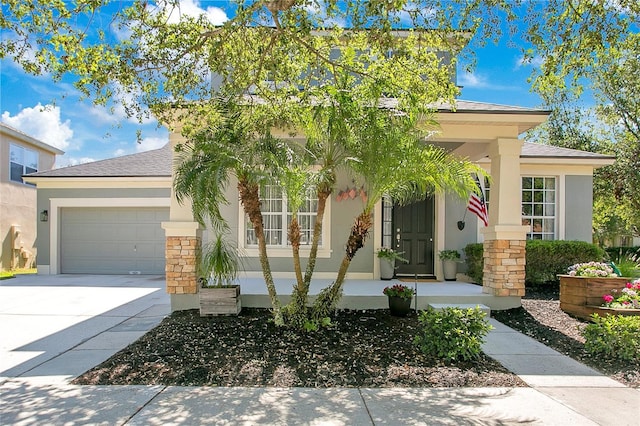 view of front of home featuring an attached garage, stone siding, covered porch, stucco siding, and driveway
