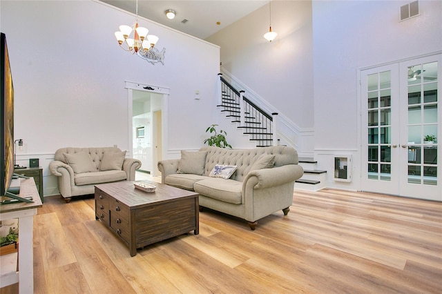 living room featuring light wood-style flooring, a towering ceiling, visible vents, stairway, and a chandelier