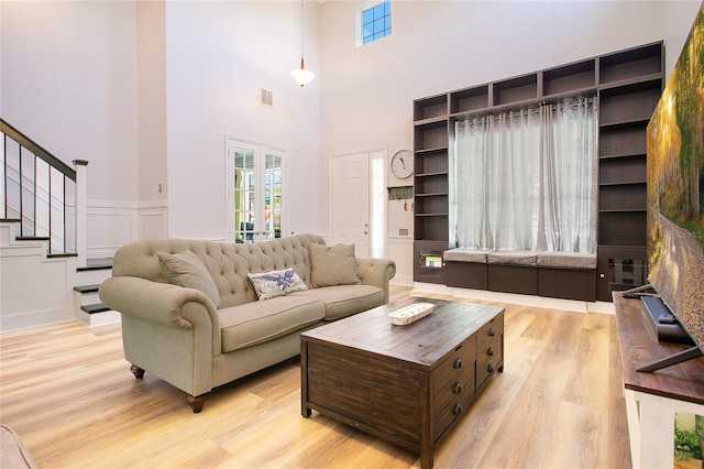 living room featuring light wood-style floors, a towering ceiling, visible vents, and stairs