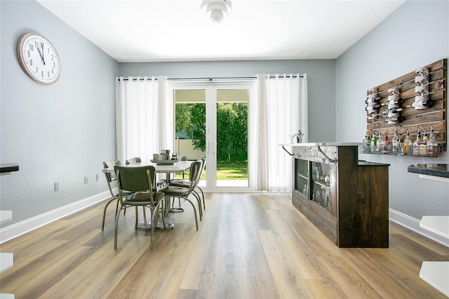 dining room with a bar, wood finished floors, and baseboards