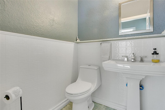 bathroom featuring a textured wall, a wainscoted wall, tile walls, and toilet