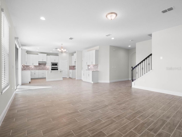 16195 Point Rock Dr, Winter Garden, FL 34787 - unfurnished living room with baseboards, an inviting chandelier, light wood-style flooring, stairs, and visible vents