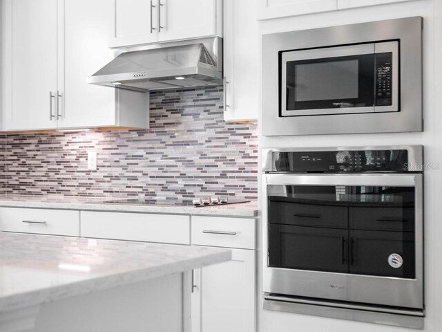 16195 Point Rock Dr, Winter Garden, FL 34787 - kitchen featuring tasteful backsplash, white cabinets, exhaust hood, appliances with stainless steel finishes, and light stone counters