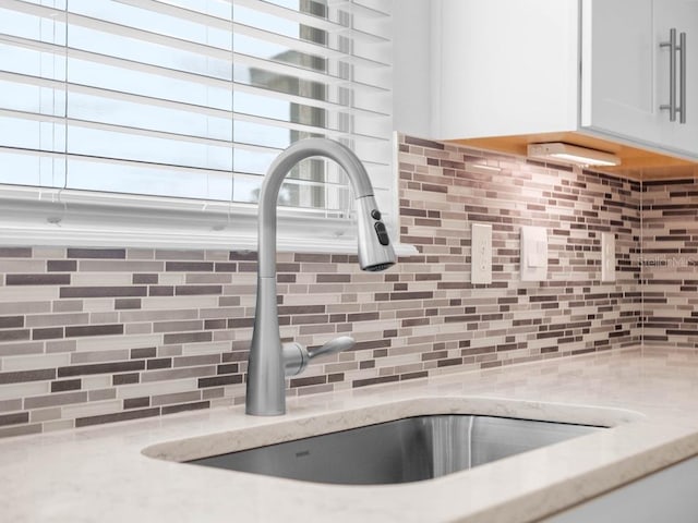 16195 Point Rock Dr, Winter Garden, FL 34787 - interior details featuring a sink, decorative backsplash, white cabinets, and light stone countertops