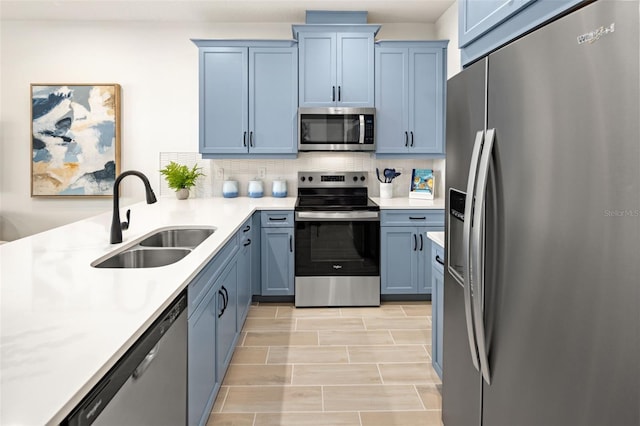kitchen with a sink, light countertops, backsplash, stainless steel appliances, and blue cabinets