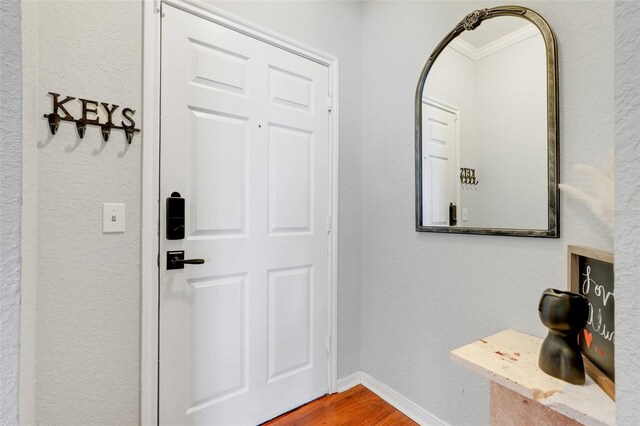 foyer featuring baseboards, ornamental molding, a textured wall, and wood finished floors