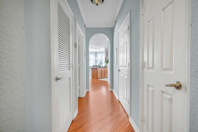 hallway with arched walkways, a sink, baseboards, light wood finished floors, and ornamental molding