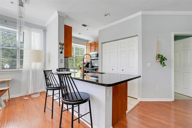 kitchen featuring crown molding, visible vents, light wood-style floors, stainless steel microwave, and a sink