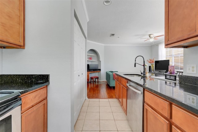 kitchen with a sink, appliances with stainless steel finishes, a ceiling fan, and dark stone countertops
