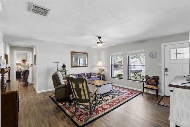 living room with visible vents, a textured ceiling, dark wood-type flooring, and ceiling fan