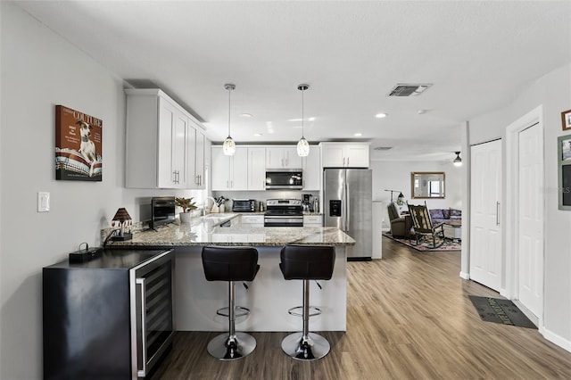 kitchen featuring light wood-style floors, white cabinetry, a peninsula, appliances with stainless steel finishes, and light stone countertops