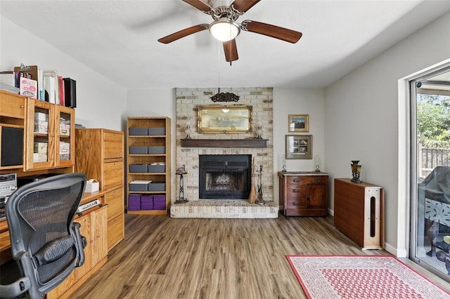 home office featuring a fireplace, wood finished floors, and ceiling fan